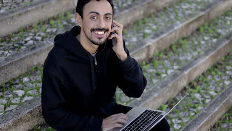 Man-with-laptop-and-smartphone-smiling-at-camera